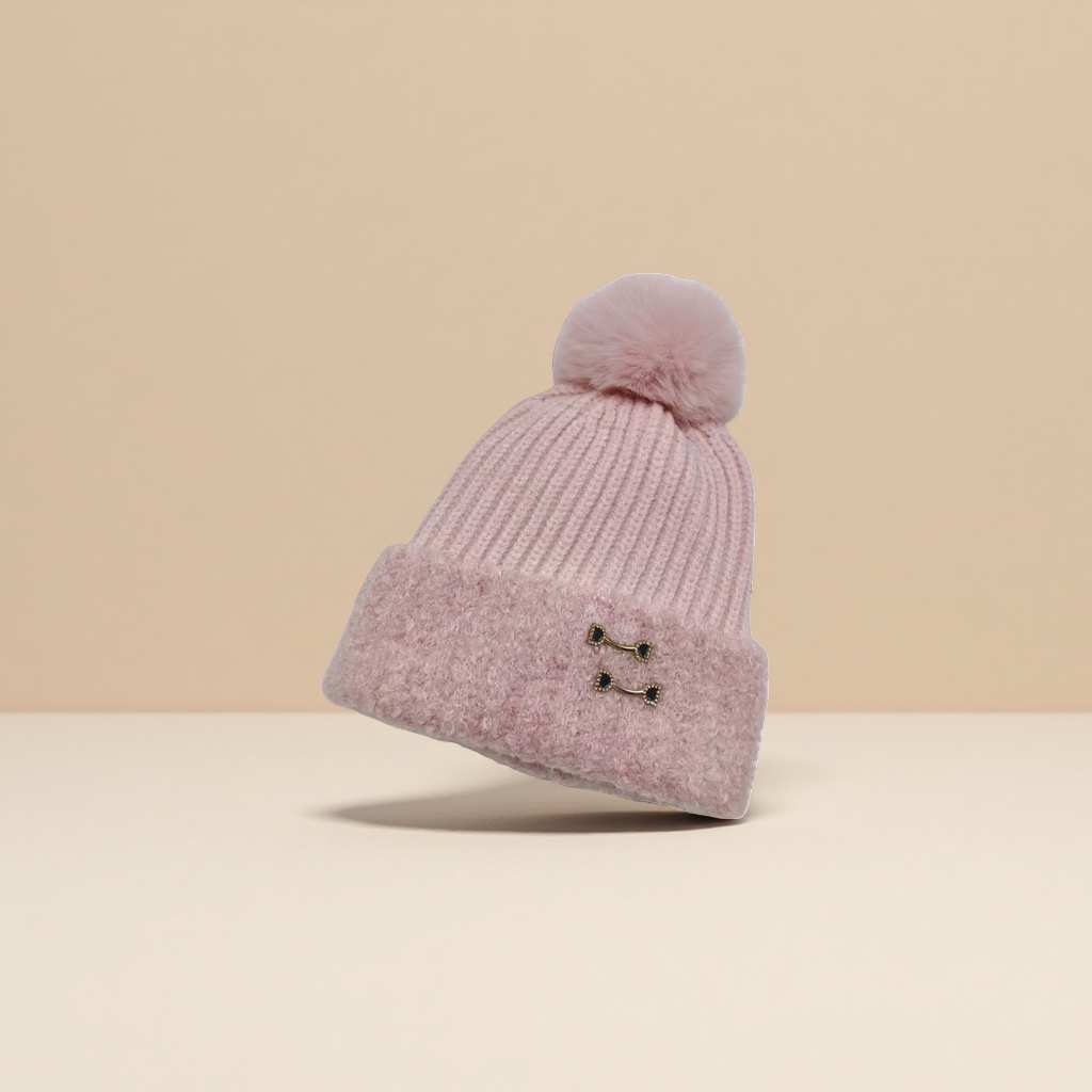 The pink woolen cap has a fluffy ball on the top, a brim and black gold metal fasteners