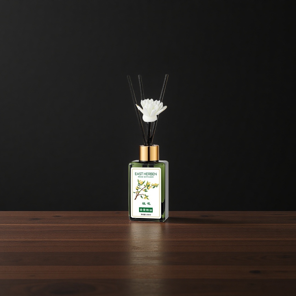 绿色玻璃瓶装香薰精油+黑色香薰棒，瓶身贴有“EAST HERBEN REED DIFFUSER”标签，配白色莲花造型装饰，背景为桂花枝叶特写。产品图