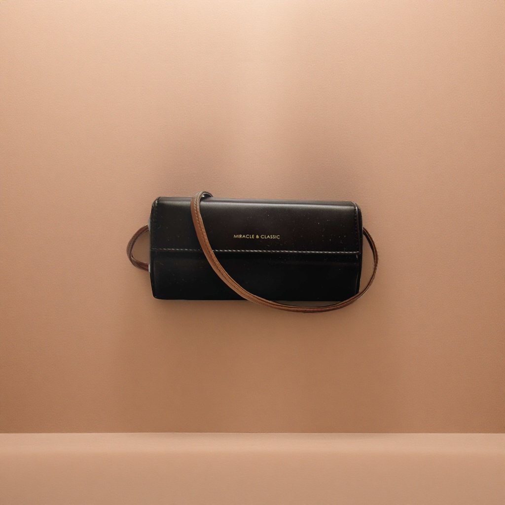 A black leather crossbody bag with a brown shoulder strap and golden MIRACLE & CLASSIC letches on the front