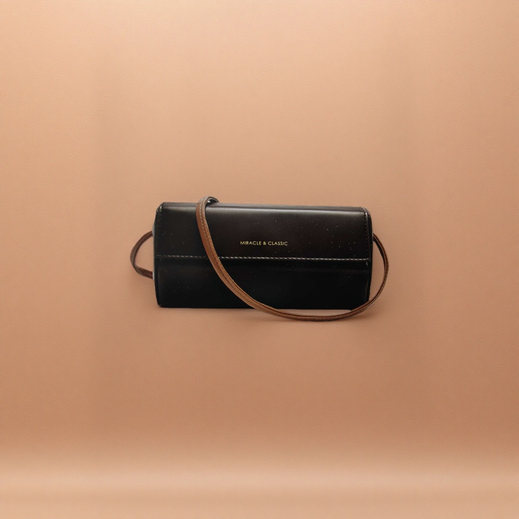 A black leather crossbody bag with a brown shoulder strap and golden MIRACLE & CLASSIC letches on the front details Picture