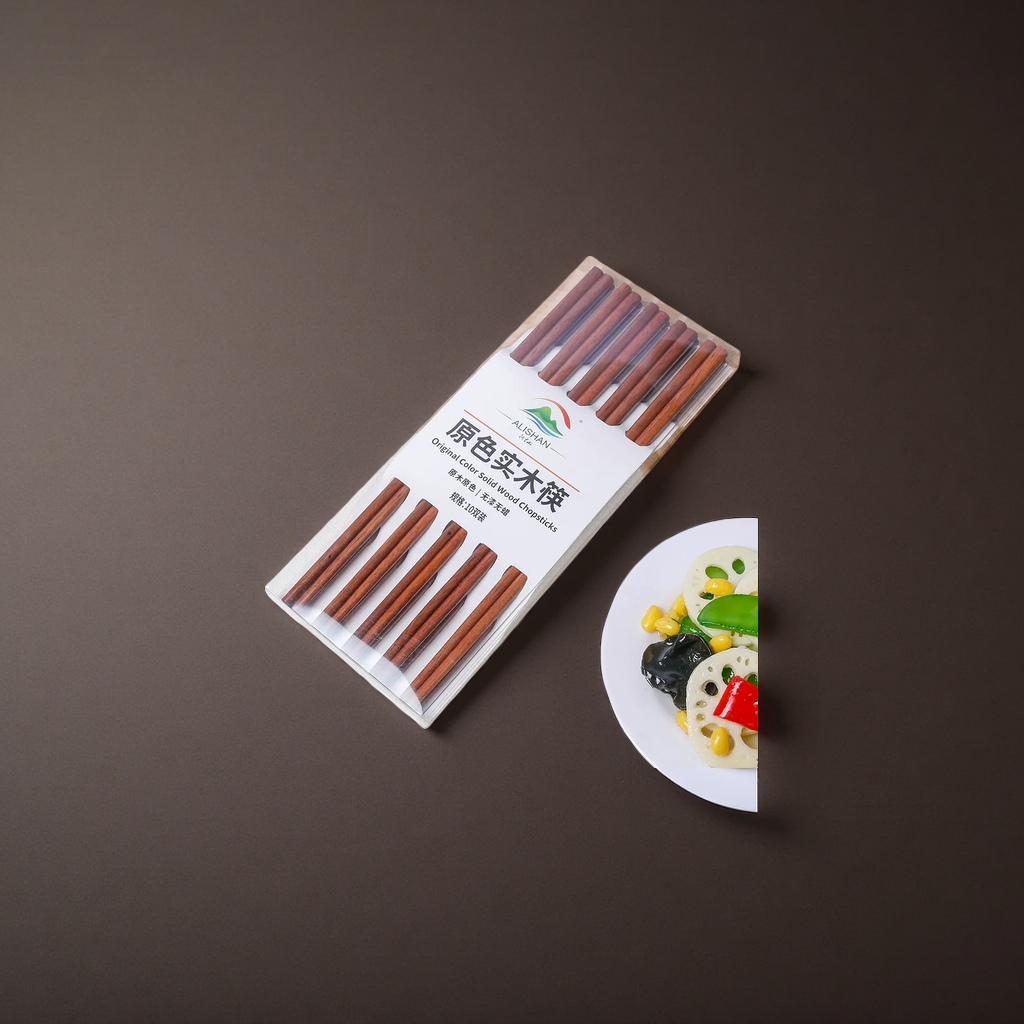 透明包装盒装的原色实木筷子，置于木质砧板旁，右下角有盛放蔬菜的白盘产品图