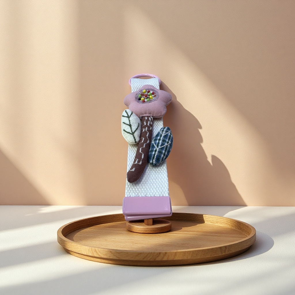 The pink flower-shaped fabric pendant is decorated with colorful beaded green leaf check patterns and white webbing connected to a pink metal ring base