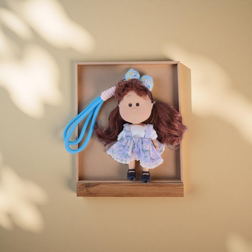 Brown curly doll, purple floral dress, black leather shoes, blue and white floral bow, grey wood grain background details Picture