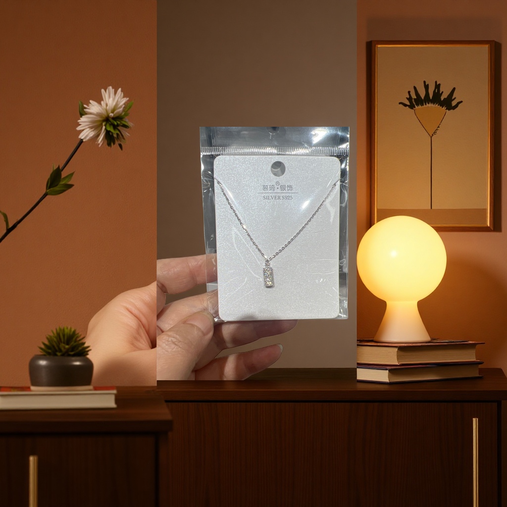 A silver full diamond rectangular pendant necklace with a fine chain, supported by white glitter cardstock for display, and packaged in transparent plastic Specification image