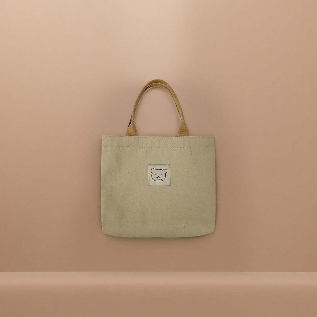 A beige canvas small bag with a brown handle and a bear face embroidered label