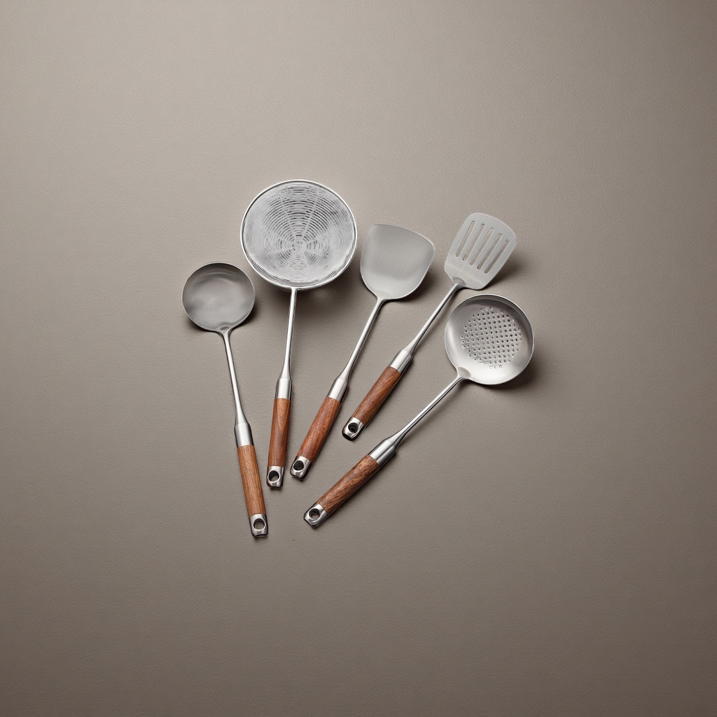 Stainless steel kitchenware set with strainer, soup spoon, spatula, wooden handle, black countertop, broccoli, mushrooms and garlic details Picture