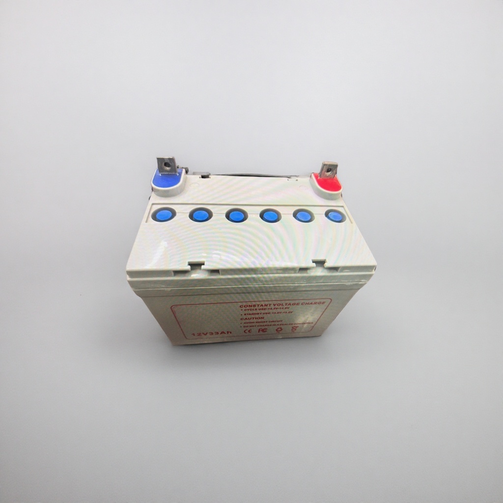 白色蓄电池，顶部有红蓝接线柱和五个蓝色观察孔，正面印有“12V33Ah”及充电说明文字产品图