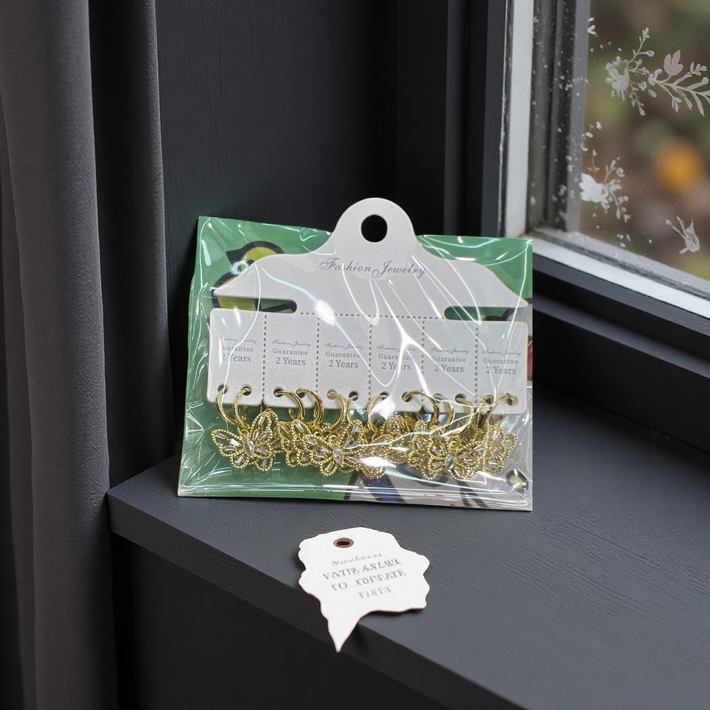 Golden butterfly-shaped earrings, packaged in a transparent plastic bag, with a white tag and a green cartoon fabric background details Picture