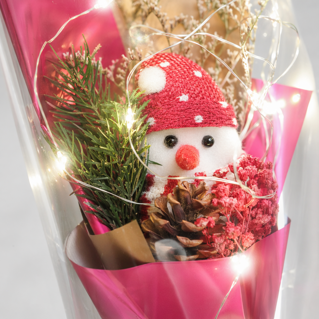 Pink packaged bouquet with snowman doll, pinecone, red berries, dried flowers, transparent bag, green ribbon and warm-colored string of lights Application Scenario