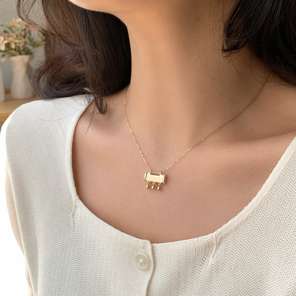 A golden rectangular small bell pendant necklace, held in a transparent bag with a white card details Picture