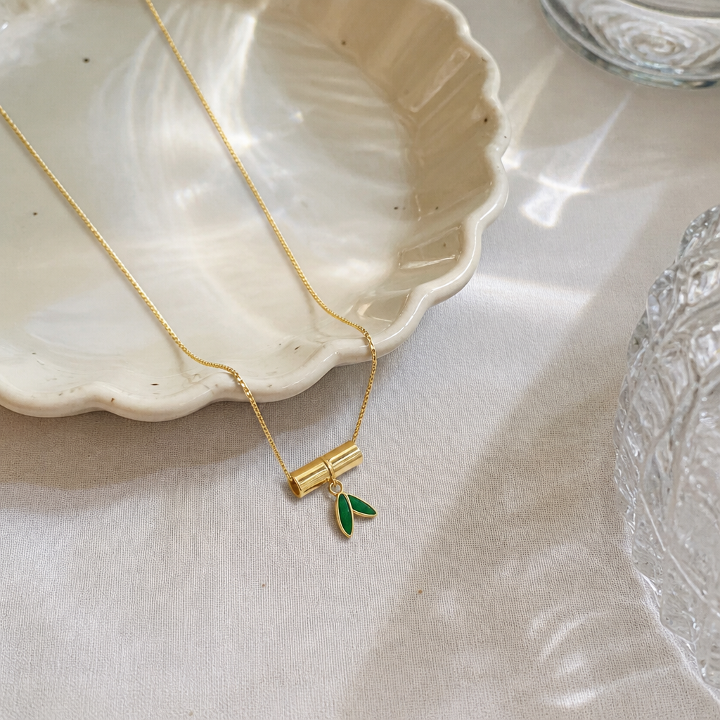 A golden bamboo pendant necklace with green leaves embellished on white cards, in a transparent bag for handheld display details Picture
