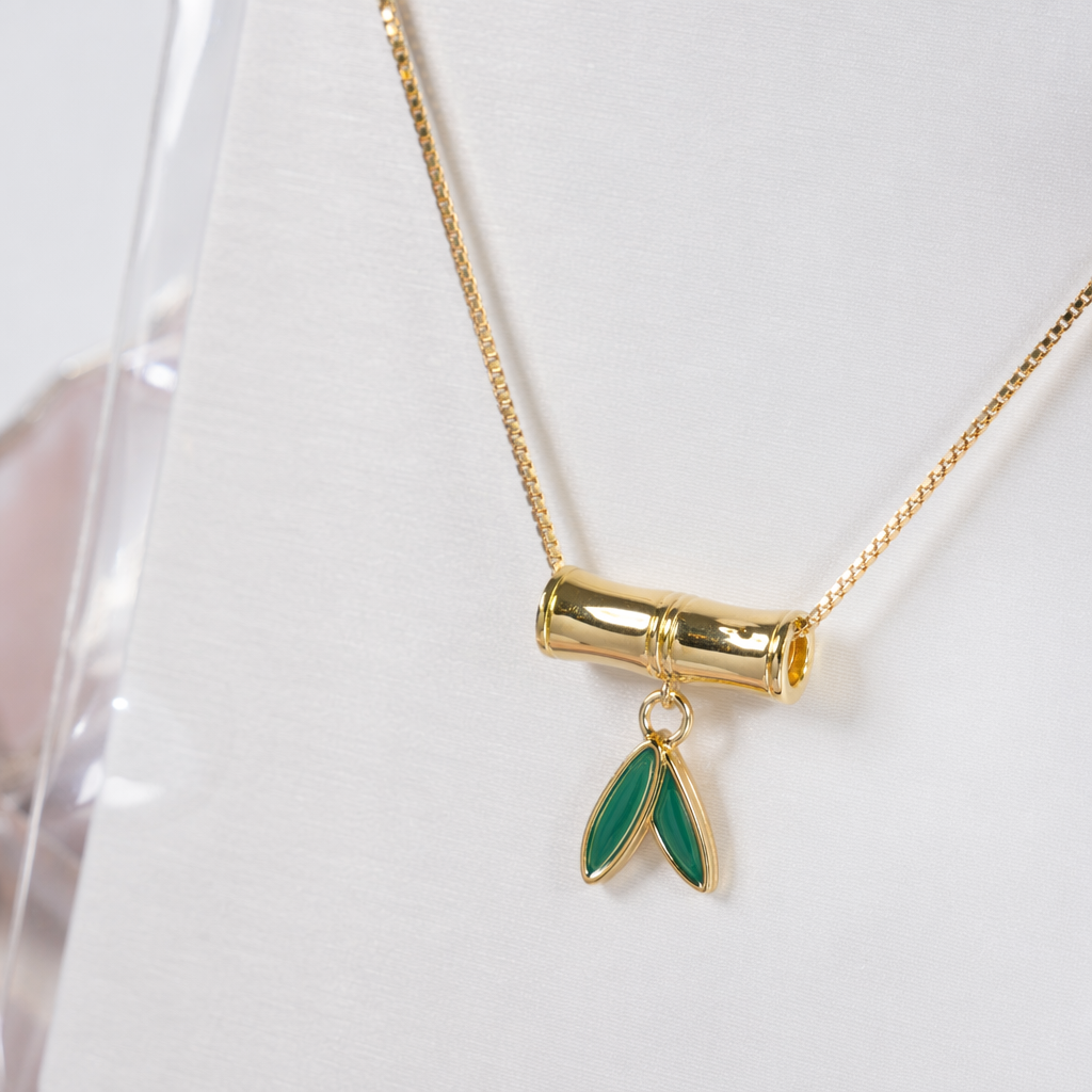A golden bamboo pendant necklace with green leaves embellished on white cards, in a transparent bag for handheld display Application Scenario