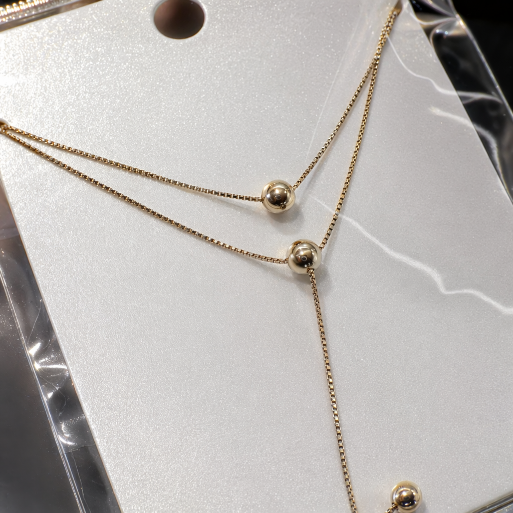 A golden double-layer spherical pendant necklace in a white card transparent bag for handheld display Application Scenario