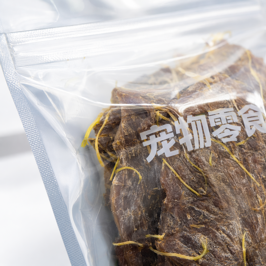 Holding a transparent bag of pet snacks, dark brown dried meat with yellow crumbs, green grass and a blue sky background Application Scenario
