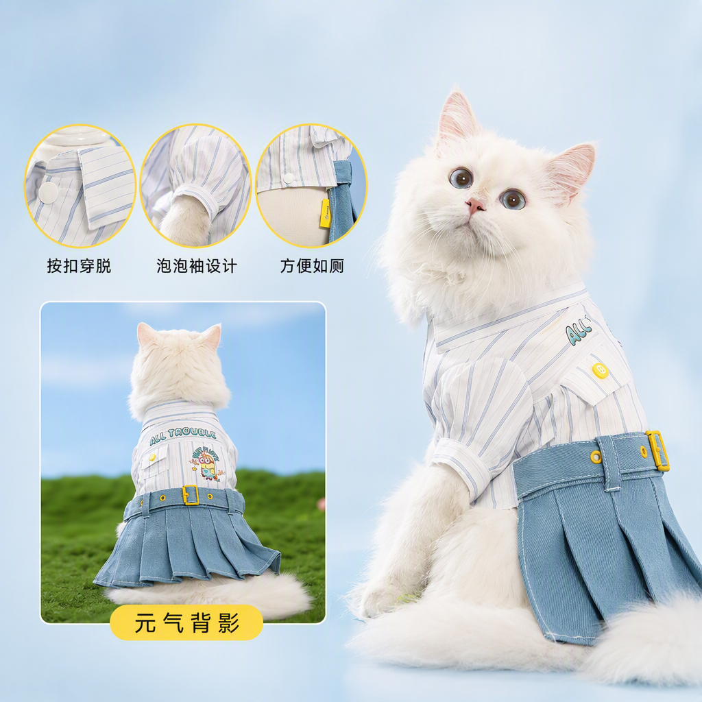 A cute long-haired cat wearing a striped shirt and a blue pleated skirt is sitting on the green grass for a casual and adorable pet photo shoot