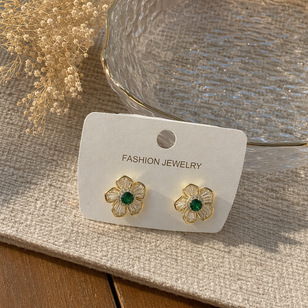 金色花朵造型耳钉，绿色宝石中心，透明水晶花瓣，附带“FASHION JEWELRY”标签的白色展示卡产品图