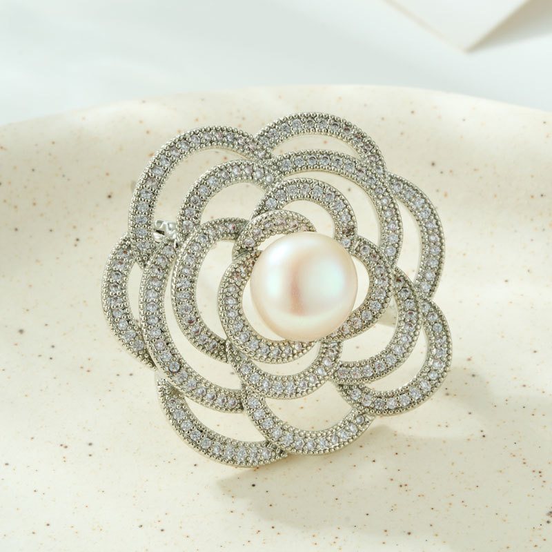 A light luxury and elegant camellia brooch with a high-end feel. It features a copper alloy freshwater pearl inlaid with zircon and a three-dimensional hollowed-out brooch