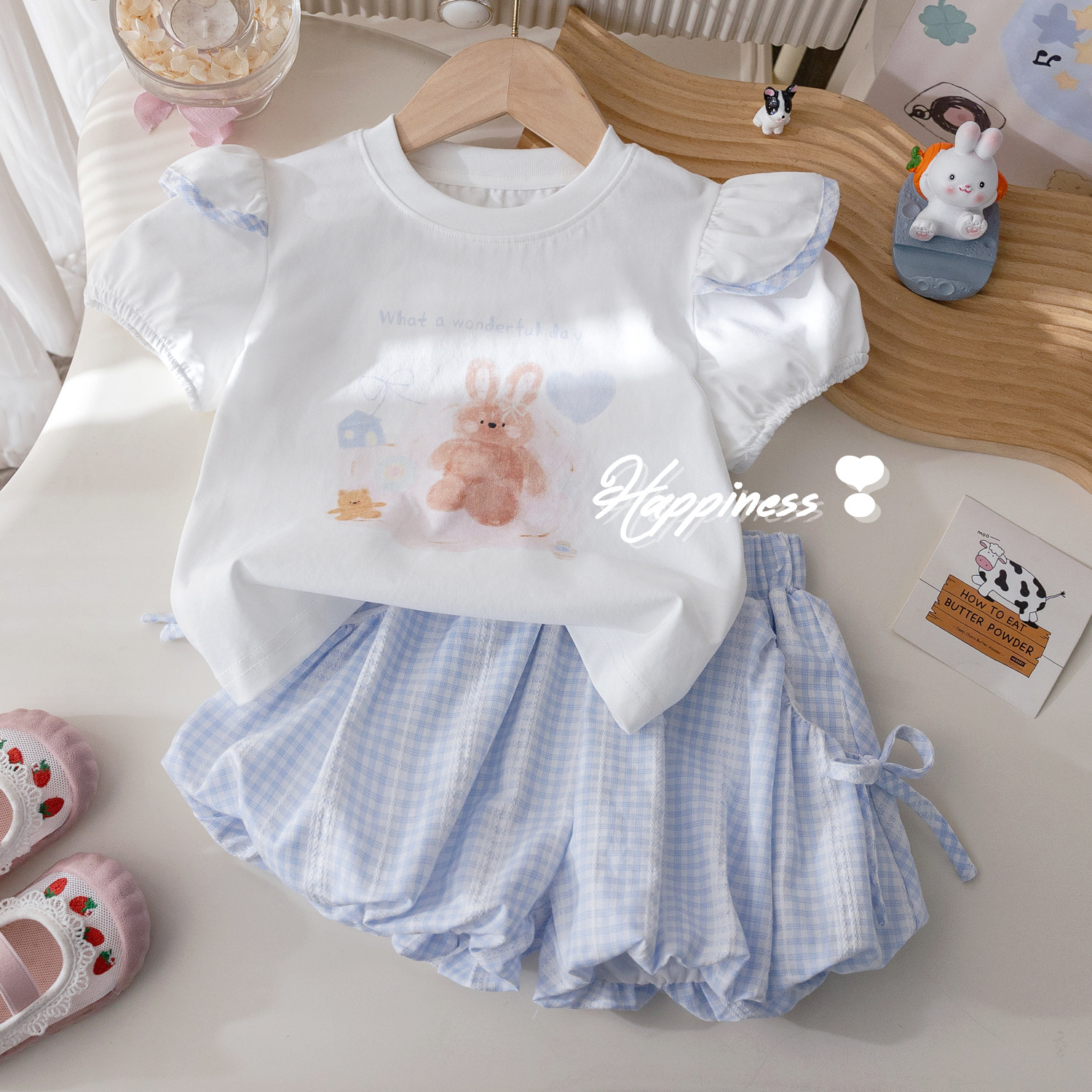 The summer new cartoon print T-shirt for girls is fashionable, and the two-piece set of checked bow flower bud pants is trendy