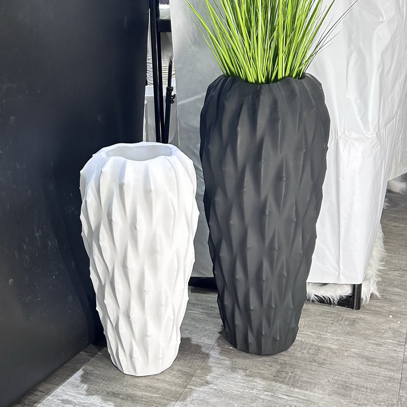 A large floor-standing plant arrangement in a minimalist style beside the sofa in the living room, featuring a new matte black and white bright color vase details Picture