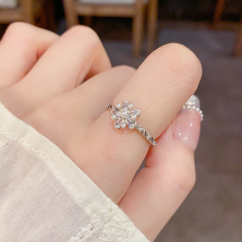 A Japanese and Korean niche diamond-encrusted pearl flower ring with an ins light luxury and high-end feel, simple and cold style. A woman who wears the ring with her mouth open