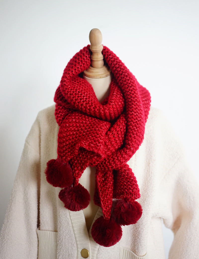 Side view of red scarf with fluffy white pom-pom gently swaying