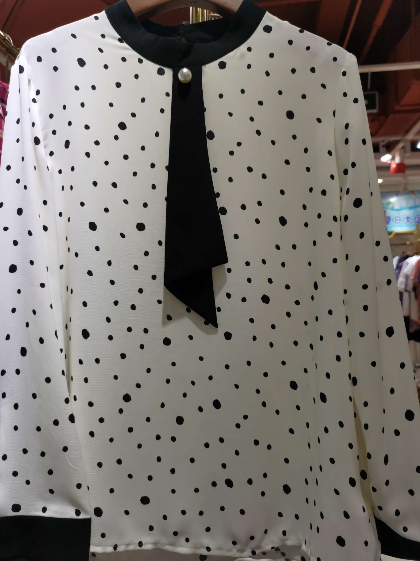 A long-sleeved women's top in pearl black with polka dots and a white background
