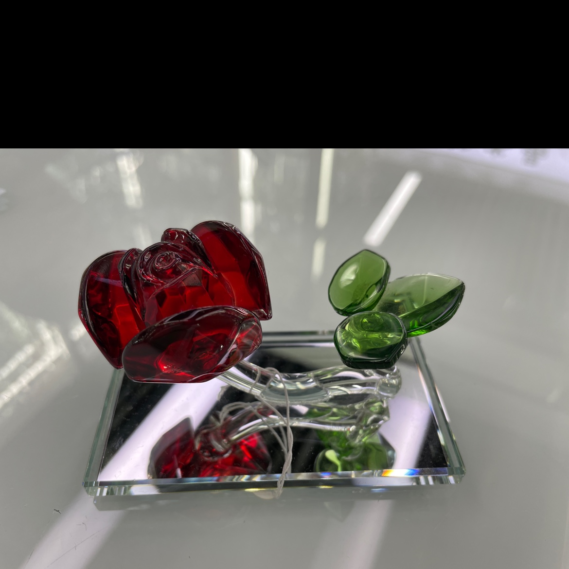 The glass decoration features rose-colored petals, transparent flower diameters and green leaves. The flower and the base are firmly fixed