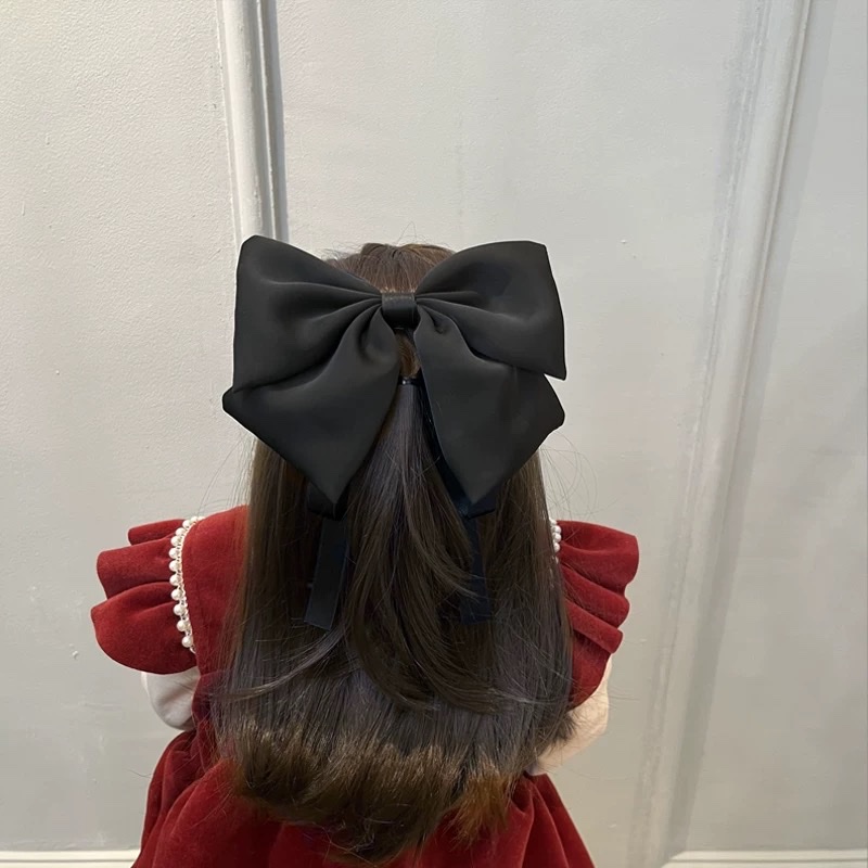 A large bow hairpin for children is stuck on the back of the head of a wine-red little girl princess for the New Year. A ribbon hairband is a cartoon hairband Application Scenario