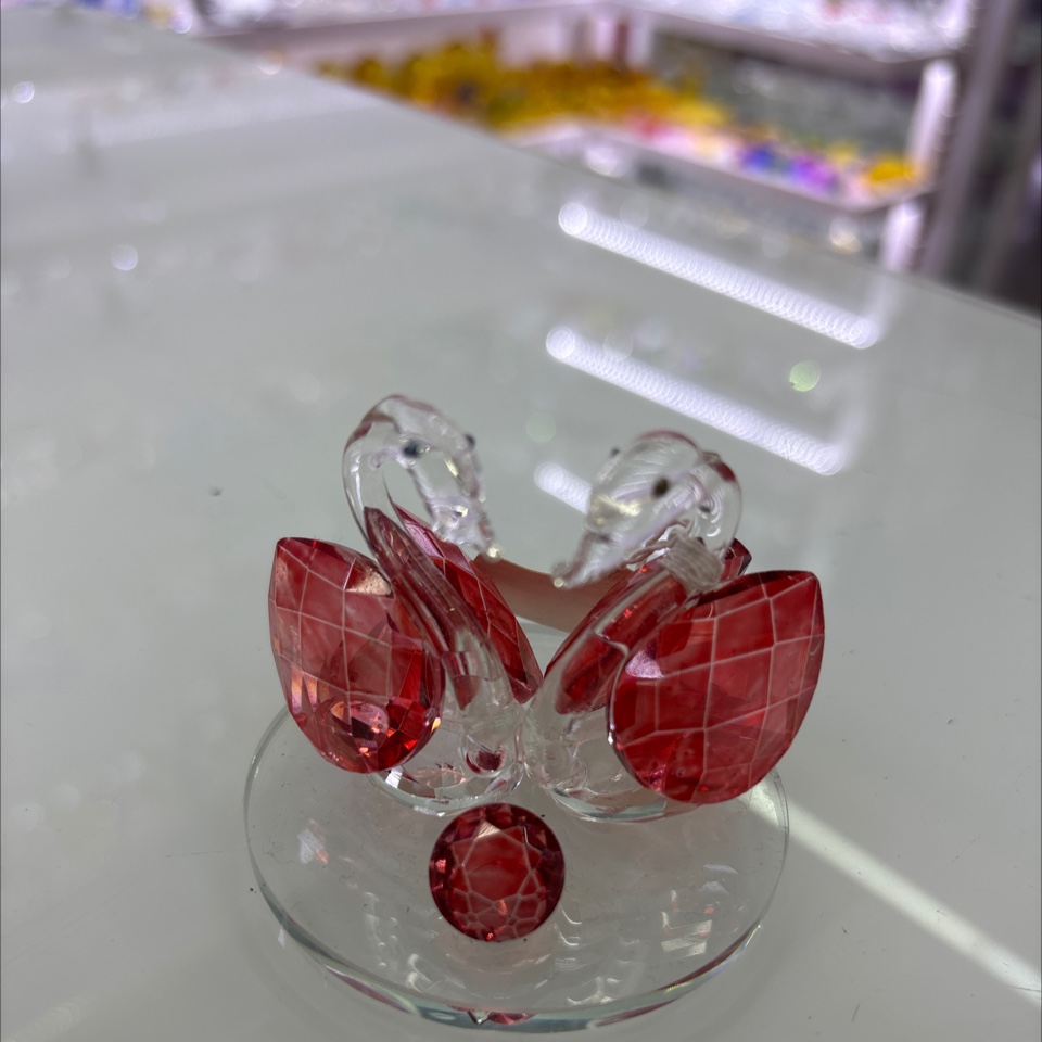 这是一个水晶天鹅摆件，属于水晶工艺品类别。其以透明水晶塑造天鹅形态，搭配红色水晶装饰，造型精致，常被用作情侣间的礼物，寓