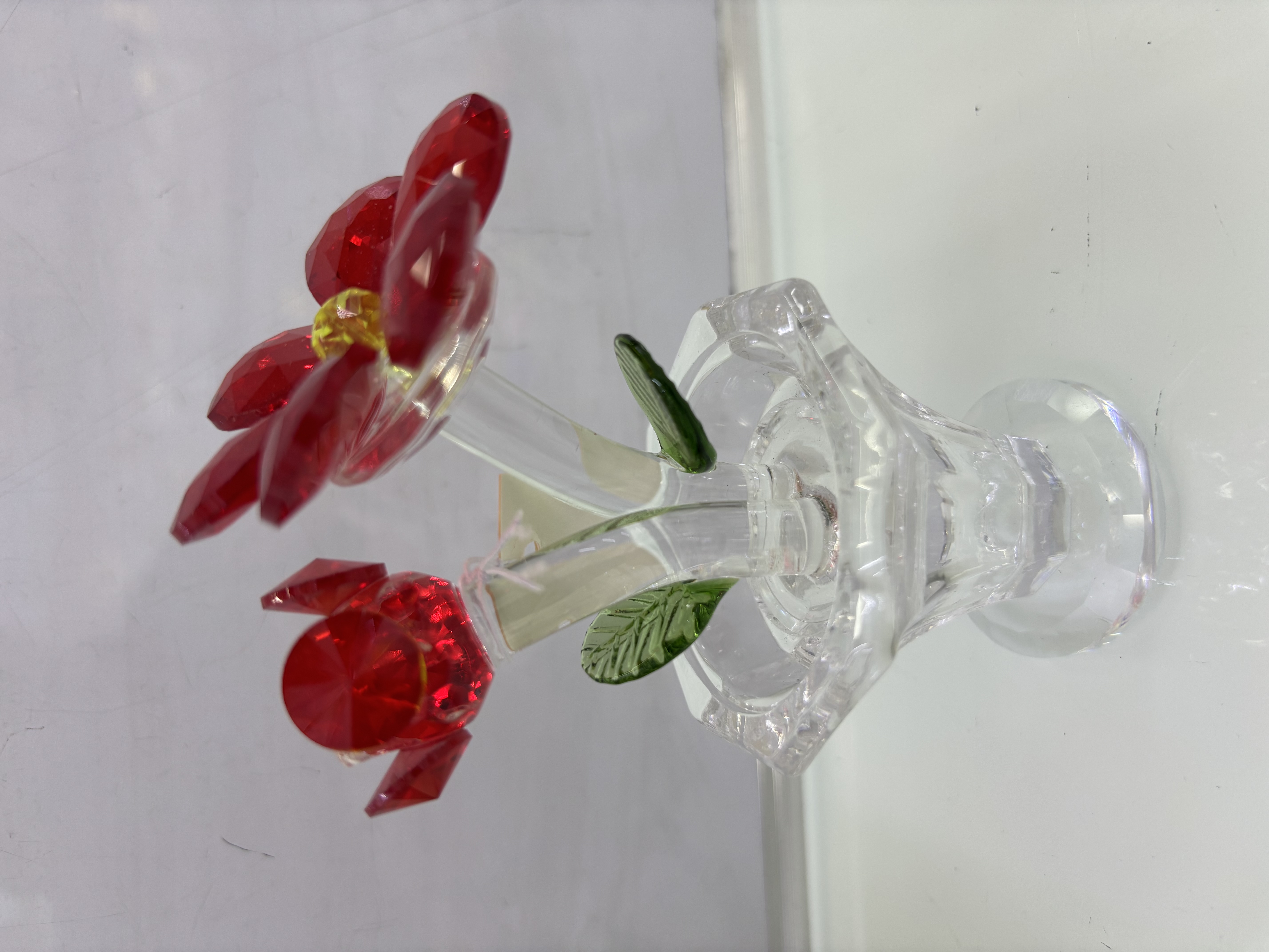 这是一个人造水晶花摆件，属于创意水晶工艺品。它以晶莹的水晶材质打造出花朵、花茎和花盆的造型，红色花瓣晶莹剔透，搭配绿色叶