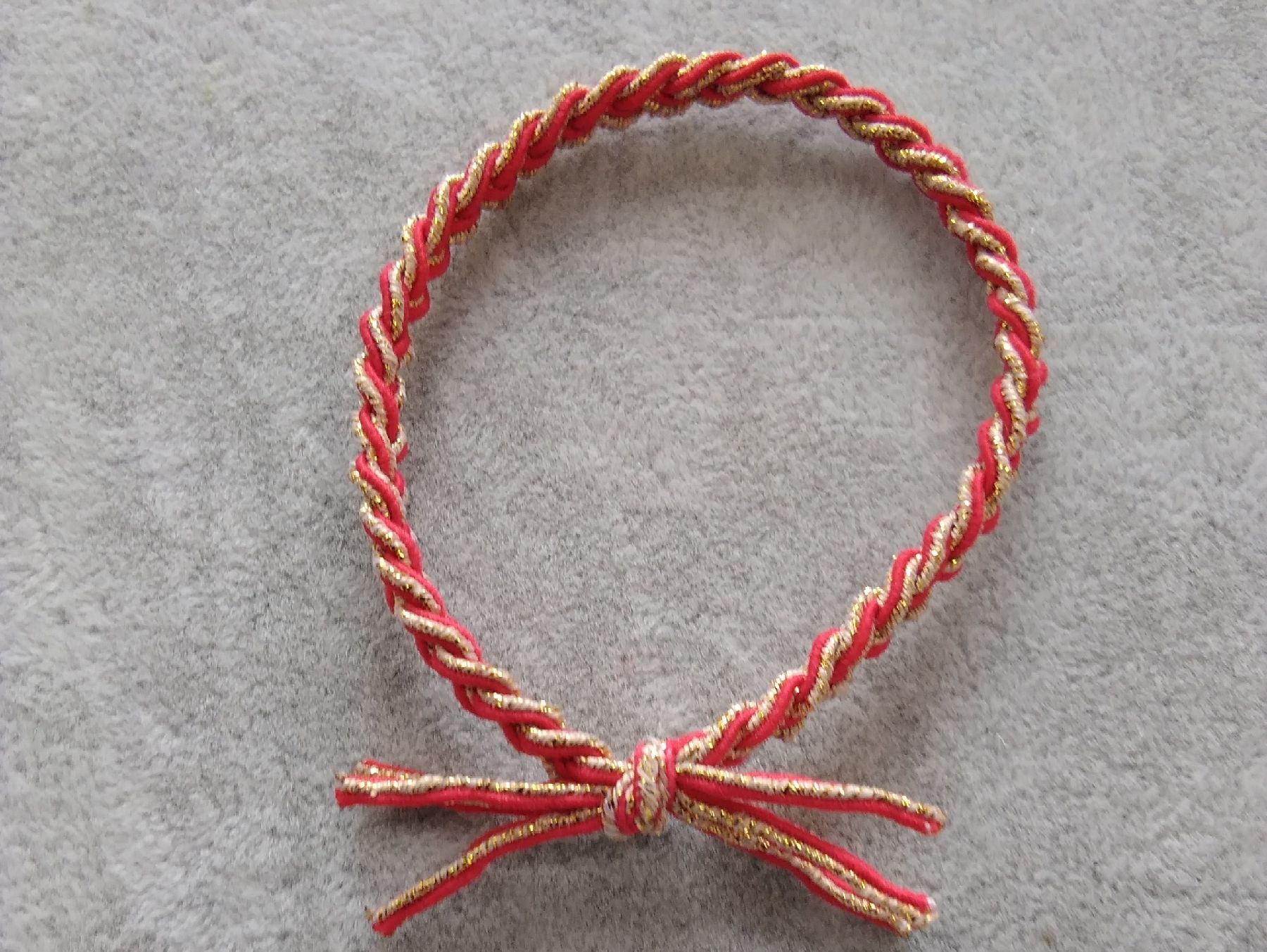 A three-strand braid with red and gold threads tied with a rubber band