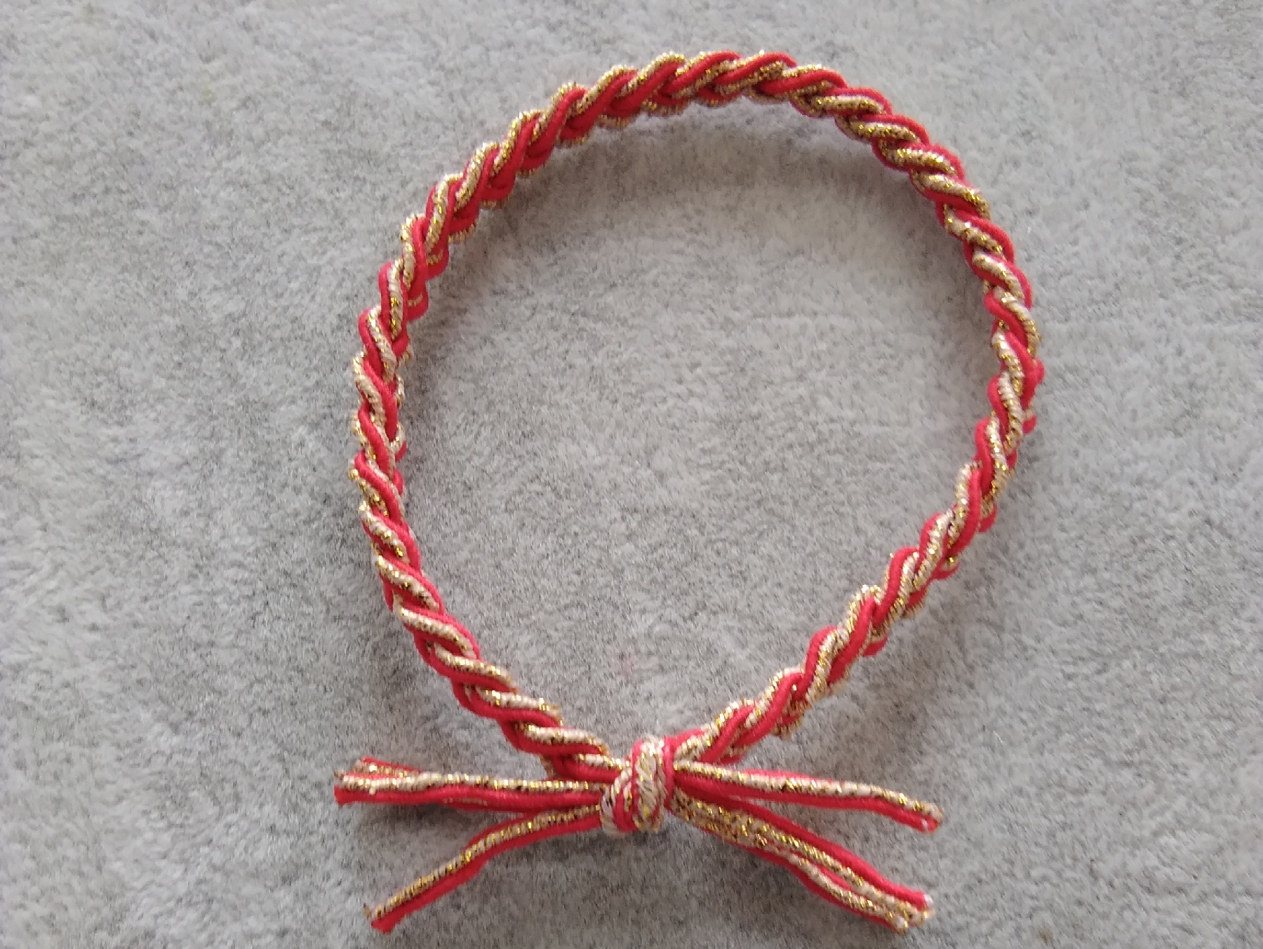 A three-strand braid with red and gold threads tied with a rubber band detail image 1