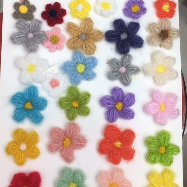 Assortment of handmade yarn flowers in vases and small pots on a white background