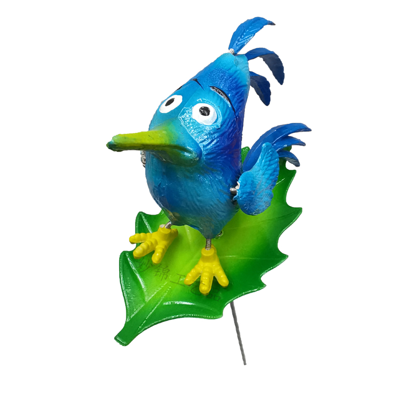 Three-tailed bird decor installed in a flower bed with surrounding greenery