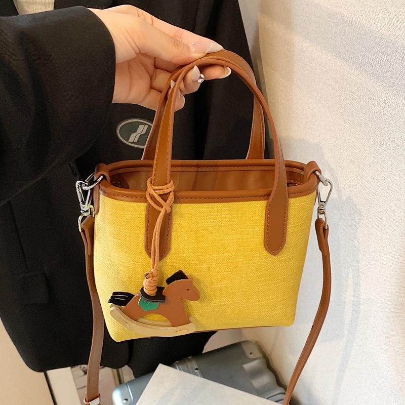 A simple and stylish hand-held bucket bag for women in the summer of 2025 with a Korean color scheme. It is a single-shoulder crossbody bag full figure