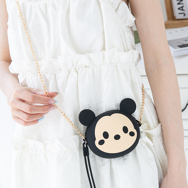 A cute and petite Korean girl's mini zipper wrist cartoon silicone coin purse is slung diagonally across a small bag for storing coins full figure
