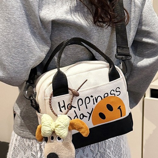A cute smiling girl handbag carried out by hand, with a high level of appearance. A canvas bag with Korean-style prints and a trendy single-shoulder crossbody bag details Picture