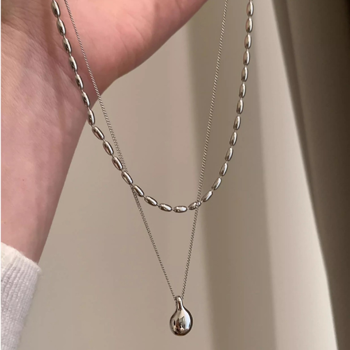 A minimalist silver double-layer necklace with a niche design for women, exuding a simple and elegant charm. It features a water drop pendant and a rice-grain collarbone chain Application Scenario