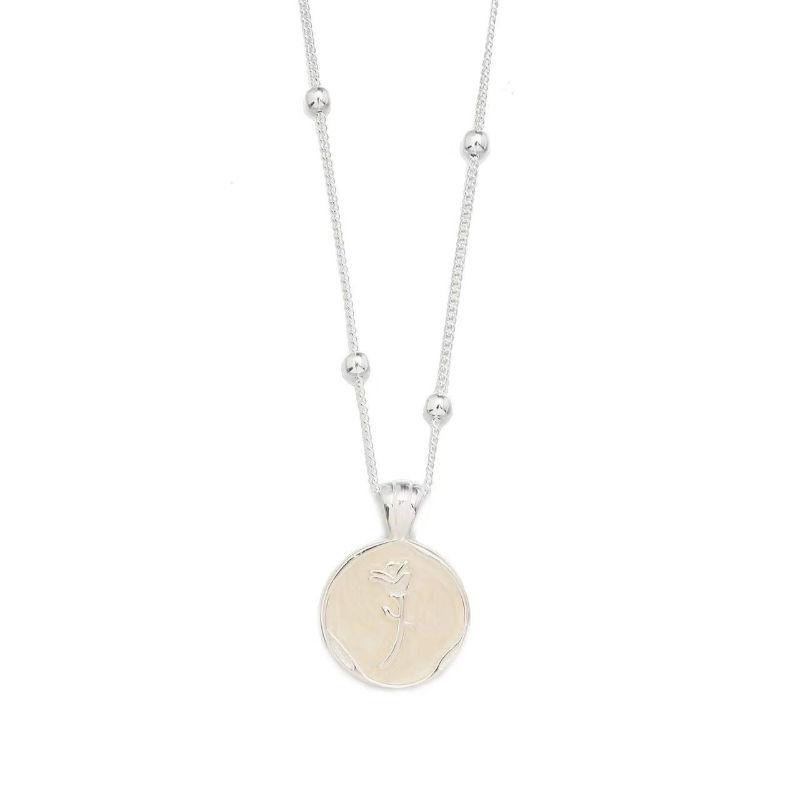 The simple silver jewelry necklace with a round pendant engraved with a dancer pattern is placed on a dark earthenware plate, exuding elegance and artistry Item Picture