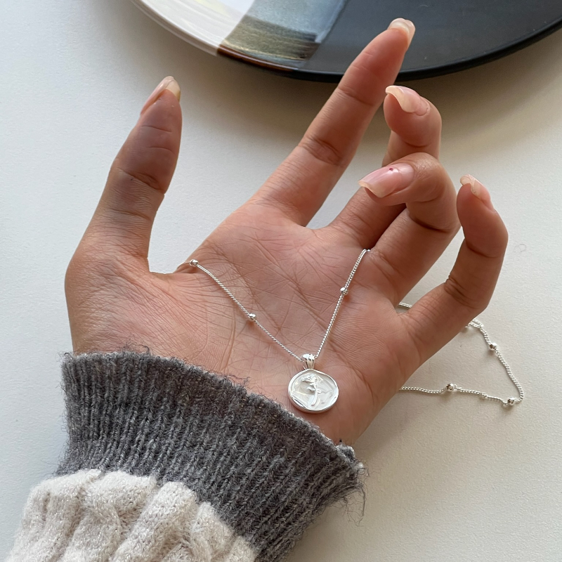 The simple silver jewelry necklace with a round pendant engraved with a dancer pattern is placed on a dark earthenware plate, exuding elegance and artistry Application Scenario