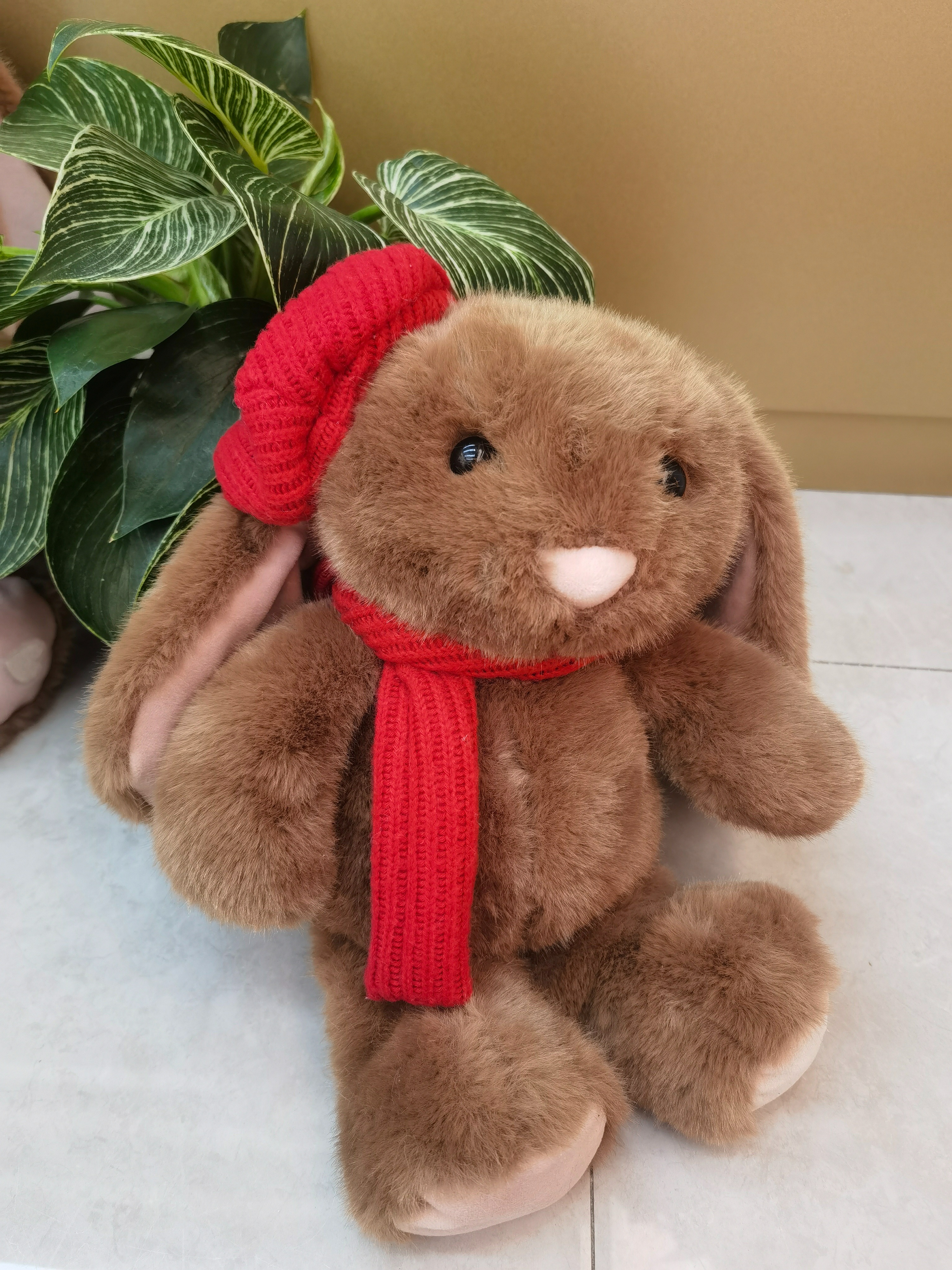 A 35CM cute rabbit wearing a red scarf and accompanied by green plants, warm and adorable.