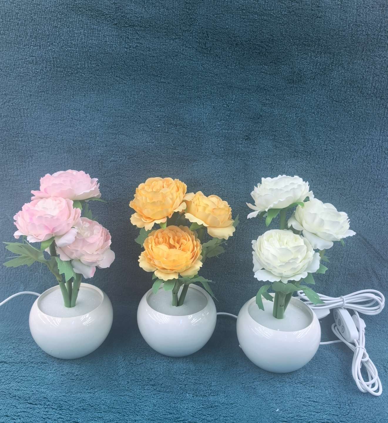 粉的柔、黄的暖、白的净，几簇仿真花窝在圆滚滚的瓷瓶里，连带着USB线都裹了温柔——把春天的软萌揣进角落，亮起来时连空气都