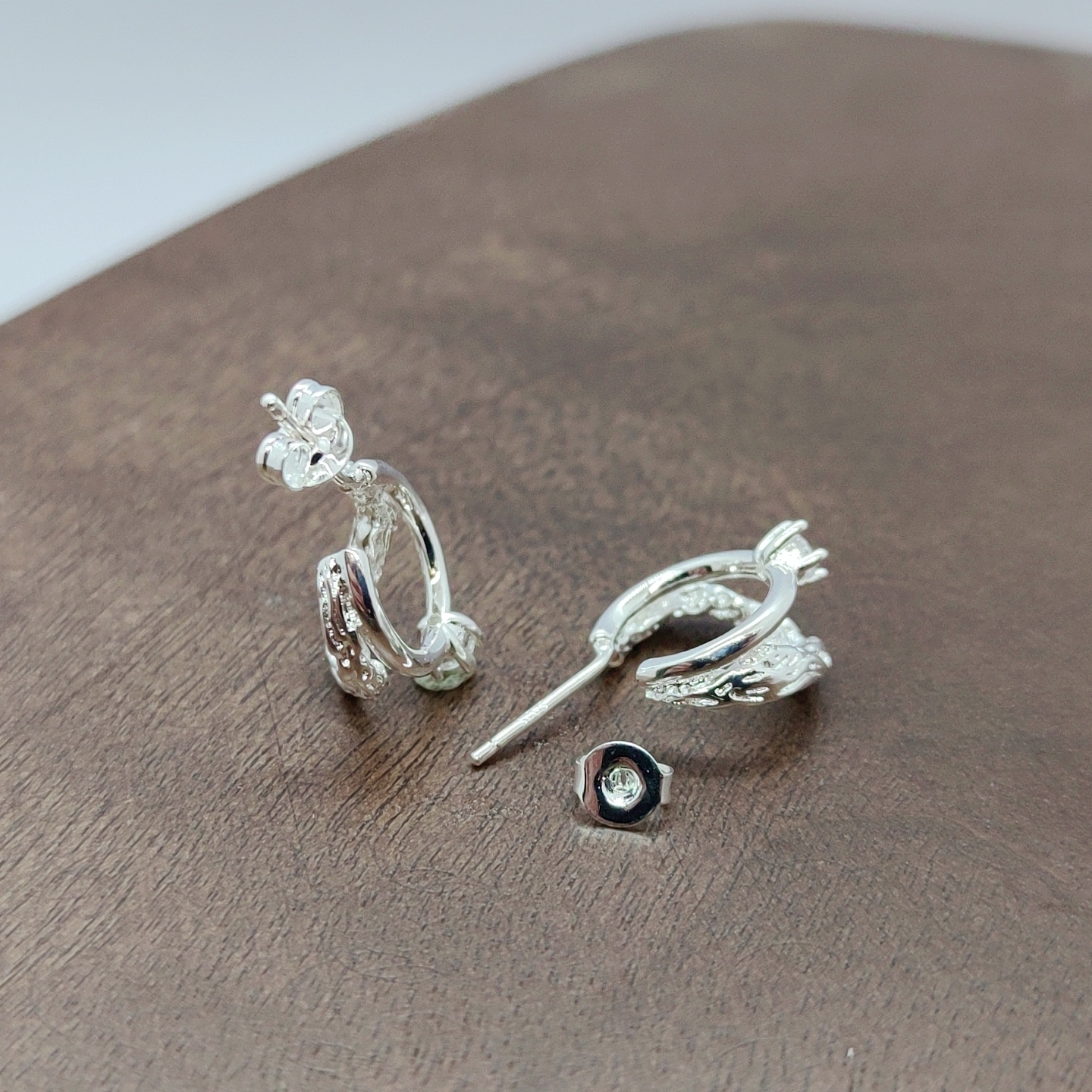 Silver earrings with exquisite patterns set with transparent gemstones, zircon micro-inlaid rough earrings placed on a wooden surface, white zirconium branch pattern earrings, and silver needles Application Scenario
