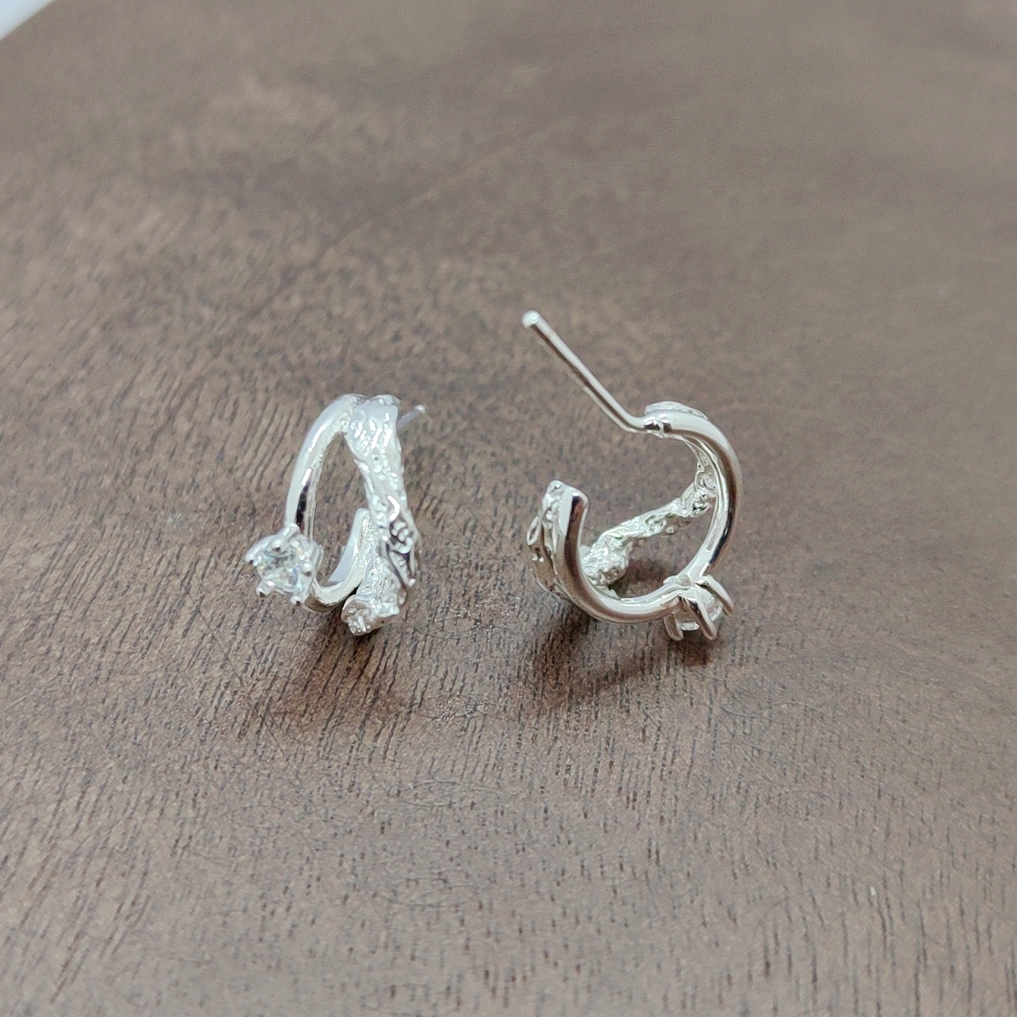 Silver earrings with exquisite patterns set with transparent gemstones, zircon micro-inlaid rough earrings placed on a wooden surface, white zirconium branch pattern earrings, and silver needles Specification image