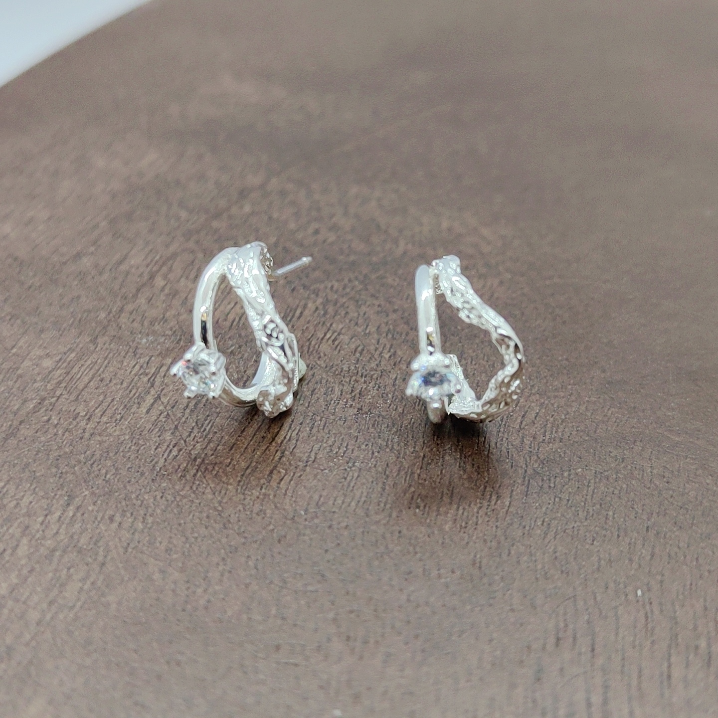 Silver earrings with exquisite patterns set with transparent gemstones, zircon micro-inlaid rough earrings placed on a wooden surface, white zirconium branch pattern earrings, and silver needles