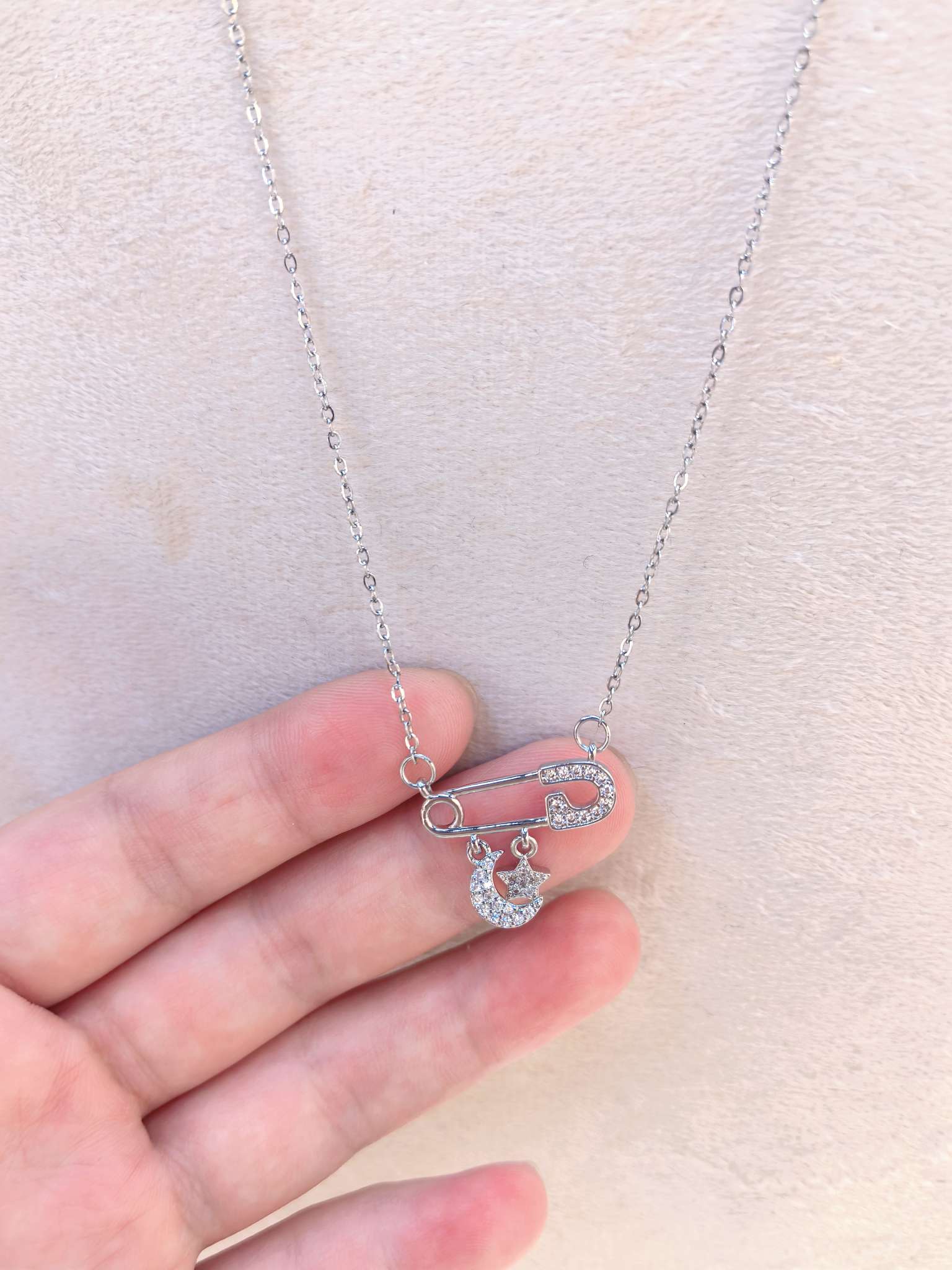 Silver safety pin necklace with diamond-encrusted moon and star pendant