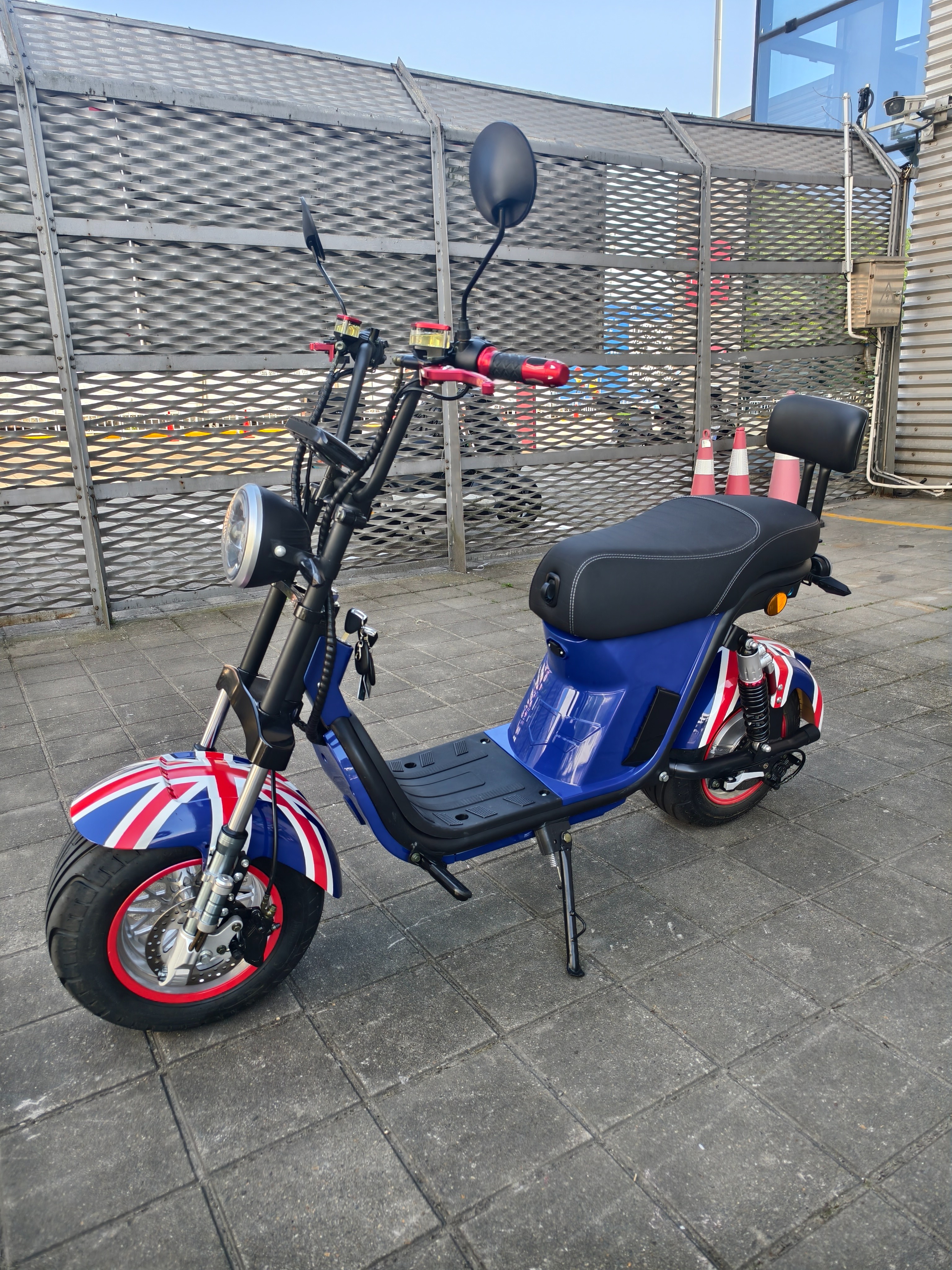 The electric vehicle features a blue British flag pattern, black seats, footrests, red handles, clear headlights and rearview mirrors details Picture