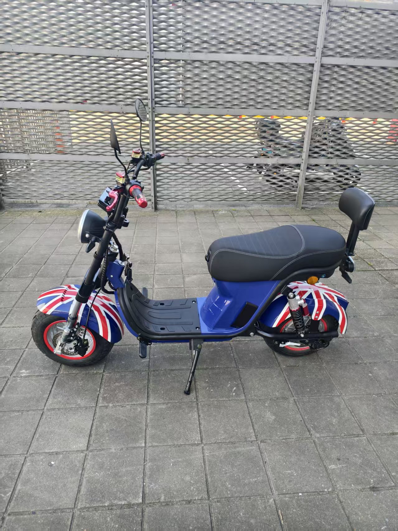 The electric vehicle features a blue British flag pattern, black seats, footrests, red handles, clear headlights and rearview mirrors Specification image