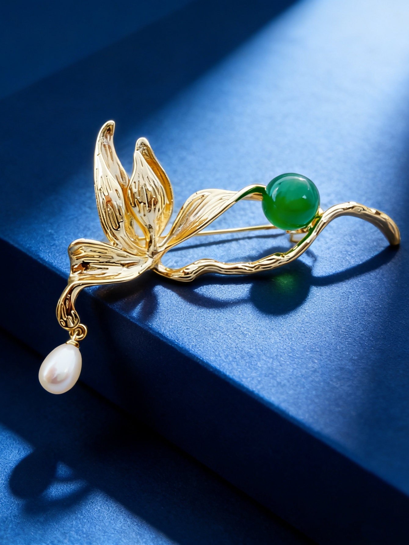 A golden leaf-shaped brooch set with green round beads, white pearls and a fashionable pin in a blue velvet box Application Scenario